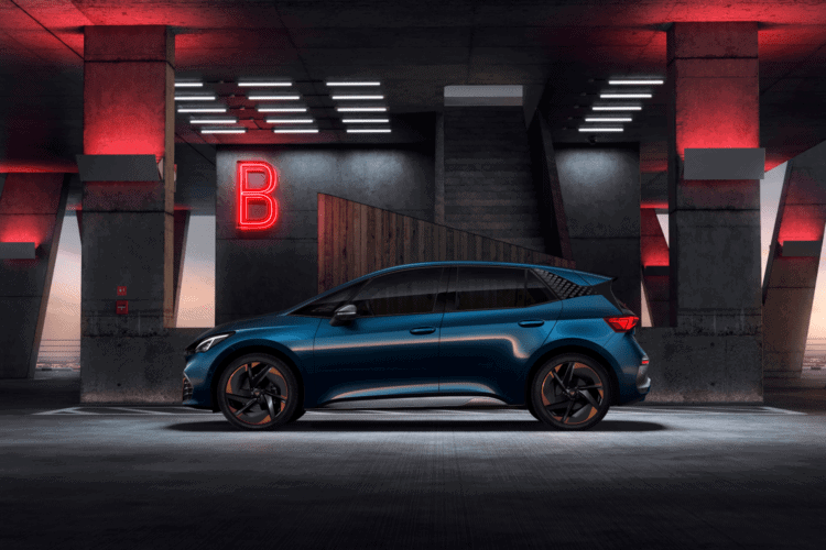 Coche eléctrico azul estacionado en un entorno urbano con iluminación moderna y señal de "B" en el f.