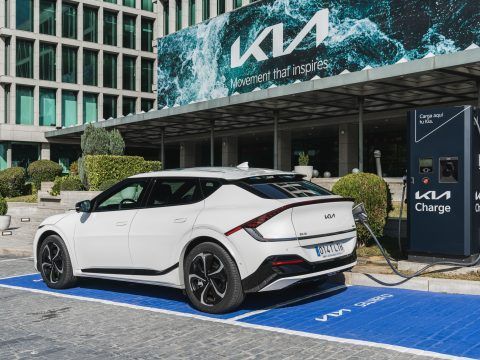 Coche eléctrico Kia cargando en estación de carga en ciudad moderna.