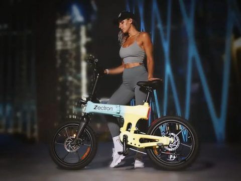 Mujer con ropa deportiva y gafas, junto a bicicleta eléctrica en entorno urbano nocturno.