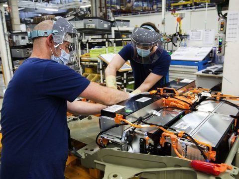 Baterías de coches eléctricos en línea de ensamblaje con técnicos inspeccionando componentes.
