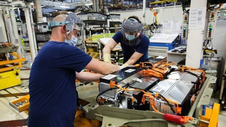 Baterías de coches eléctricos en línea de ensamblaje con técnicos inspeccionando componentes.