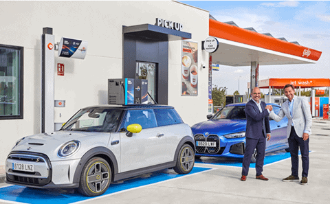 Mini coche eléctrico en estación de carga con dos hombres sonriendo y dándose la mano.