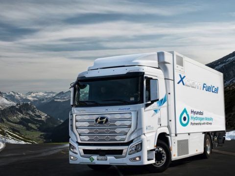 Camión eléctrico en carretera montañosa con paisaje de picos nevados y cielo nublado.