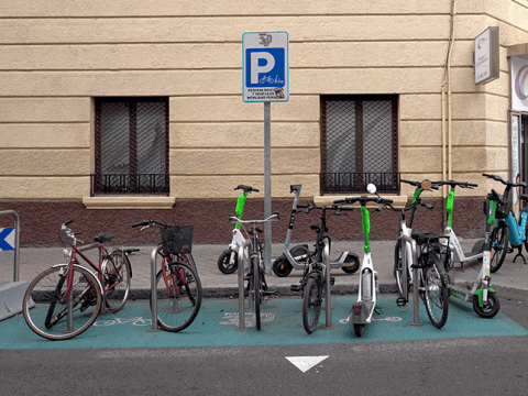Bicicletas y scooters eléctricos aparcados en zona de estacionamiento en la calle.