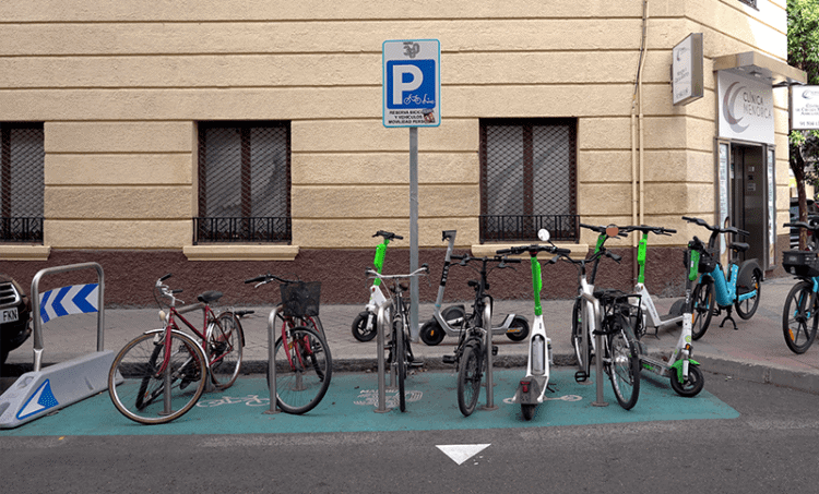 Bicicletas y scooters eléctricos aparcados en zona de estacionamiento en la calle.