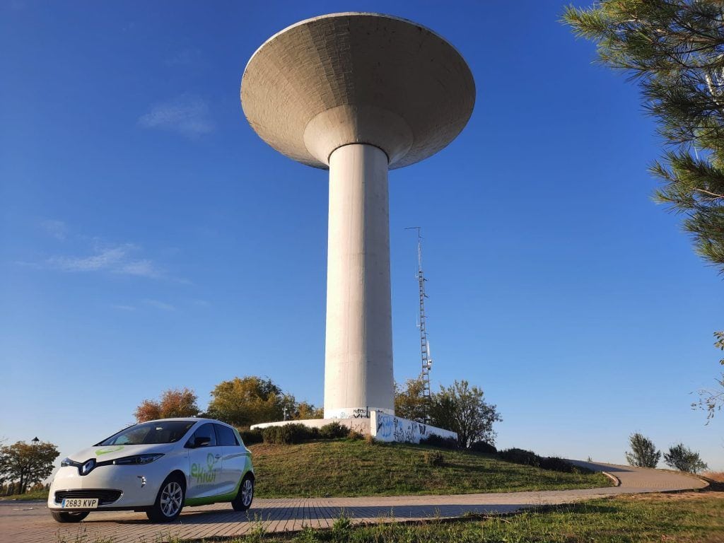 Recarga de vehículos eléctricos junto a una torre de agua en un entorno al aire libre.