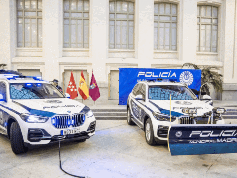 Dos coches de policía de Madrid en exhibición con escudos y banderas en un evento oficial.