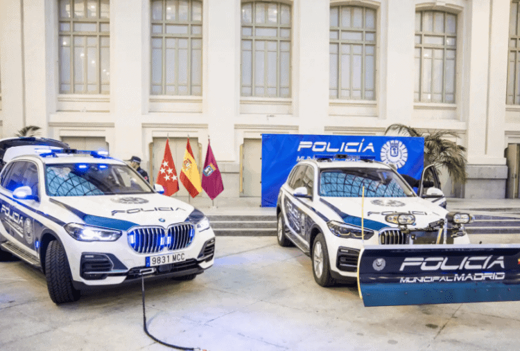 Dos coches de policía de Madrid en exhibición con escudos y banderas en un evento oficial.