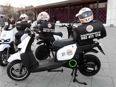 Motos eléctricas de reparto con cascos y cajas de Burger King en la ciudad.