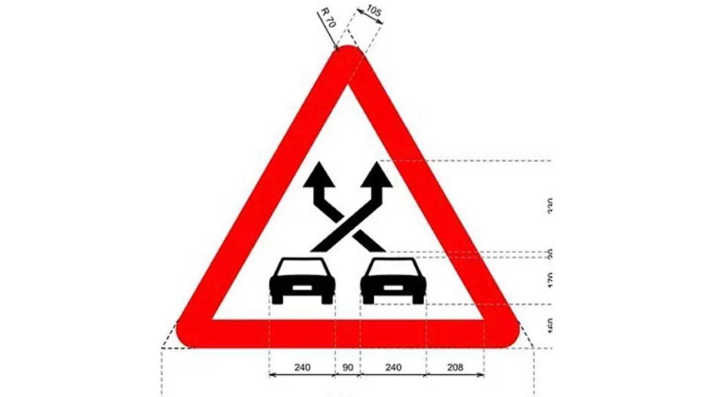 Señal de advertencia de adelantamiento en carretera con coches y flechas en un triángulo rojo.