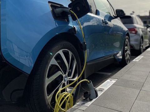 Coche eléctrico azul conectado a una estación de carga en un aparcamiento.