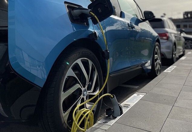 Coche eléctrico azul conectado a una estación de carga en un aparcamiento.