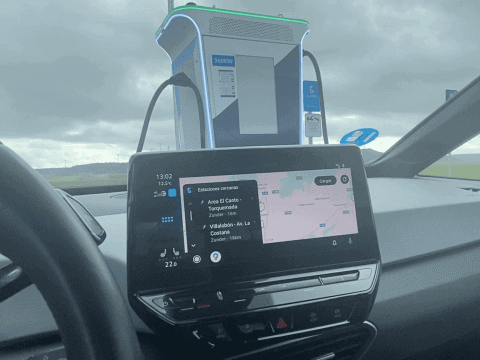 Cargador de coche eléctrico en ruta con pantalla digital y conectores en un coche en movimiento.