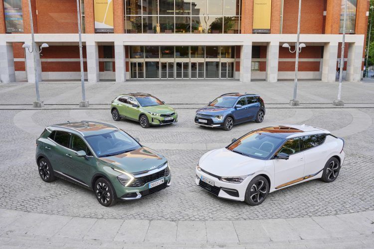 Cinco coches eléctricos en exhibición en una plaza urbana moderna.
