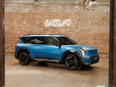 Un coche eléctrico Kia en un espacio industrial con pared de ladrillos y letrero luminoso Kia.