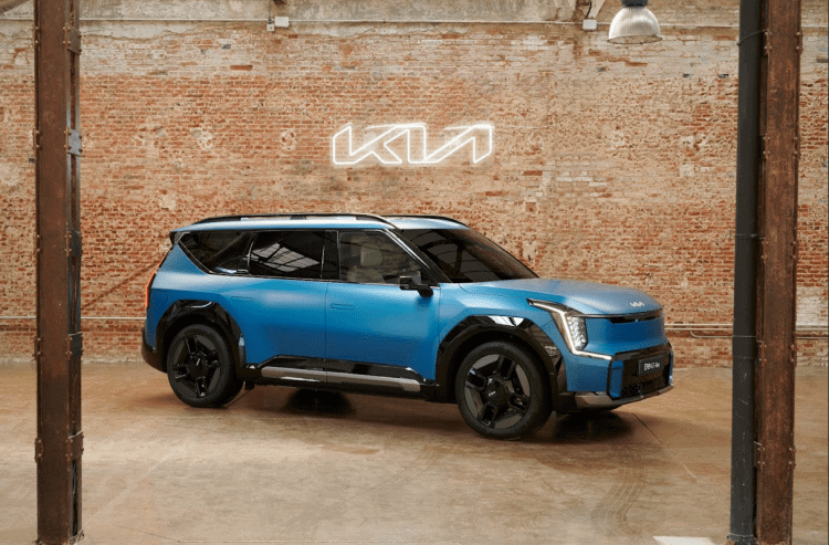 Un coche eléctrico Kia en un espacio industrial con pared de ladrillos y letrero luminoso Kia.
