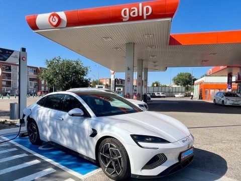 Coche eléctrico blanco cargando en estación de servicio en ciudad.