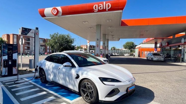Coche eléctrico blanco cargando en estación de servicio en ciudad.