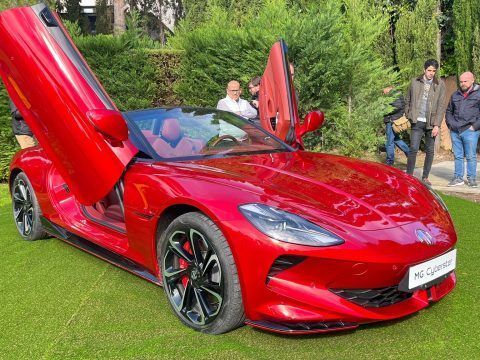 Un coche deportivo eléctrico rojo con puertas de tijera abiertas en un jardín.