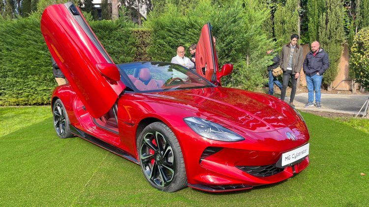 Un coche deportivo eléctrico rojo con puertas de tijera abiertas en un jardín.