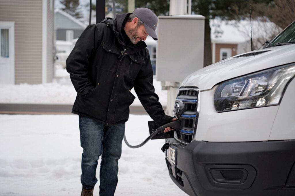 Hombre cargando un coche eléctrico en un día nevado, conectado a la estación de carga.