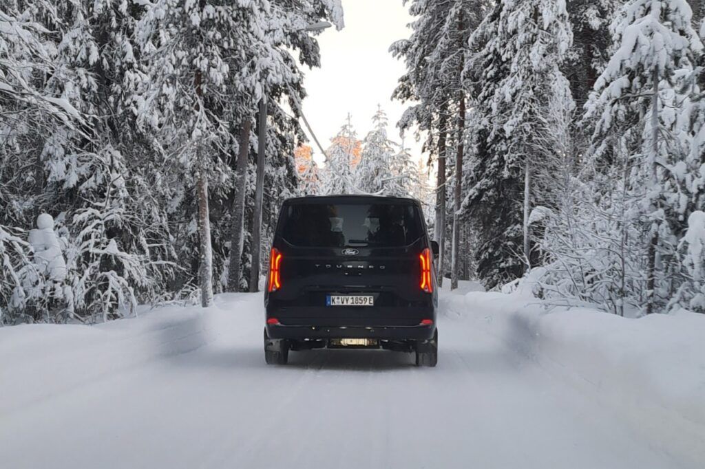 Vehículo eléctrico conduciendo por un camino cubierto de nieve en un bosque invernal.
